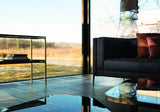 Samira luxury sofa in black leather with burnished brass legs beside floor to ceiling windows