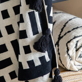 Elevate Your Home Decor with a Modern Knit Throw with Tassels. This luxuriously textured knit throw, available in black & cream or ochre & cream, adds a touch of contemporary style and comfort to any space.